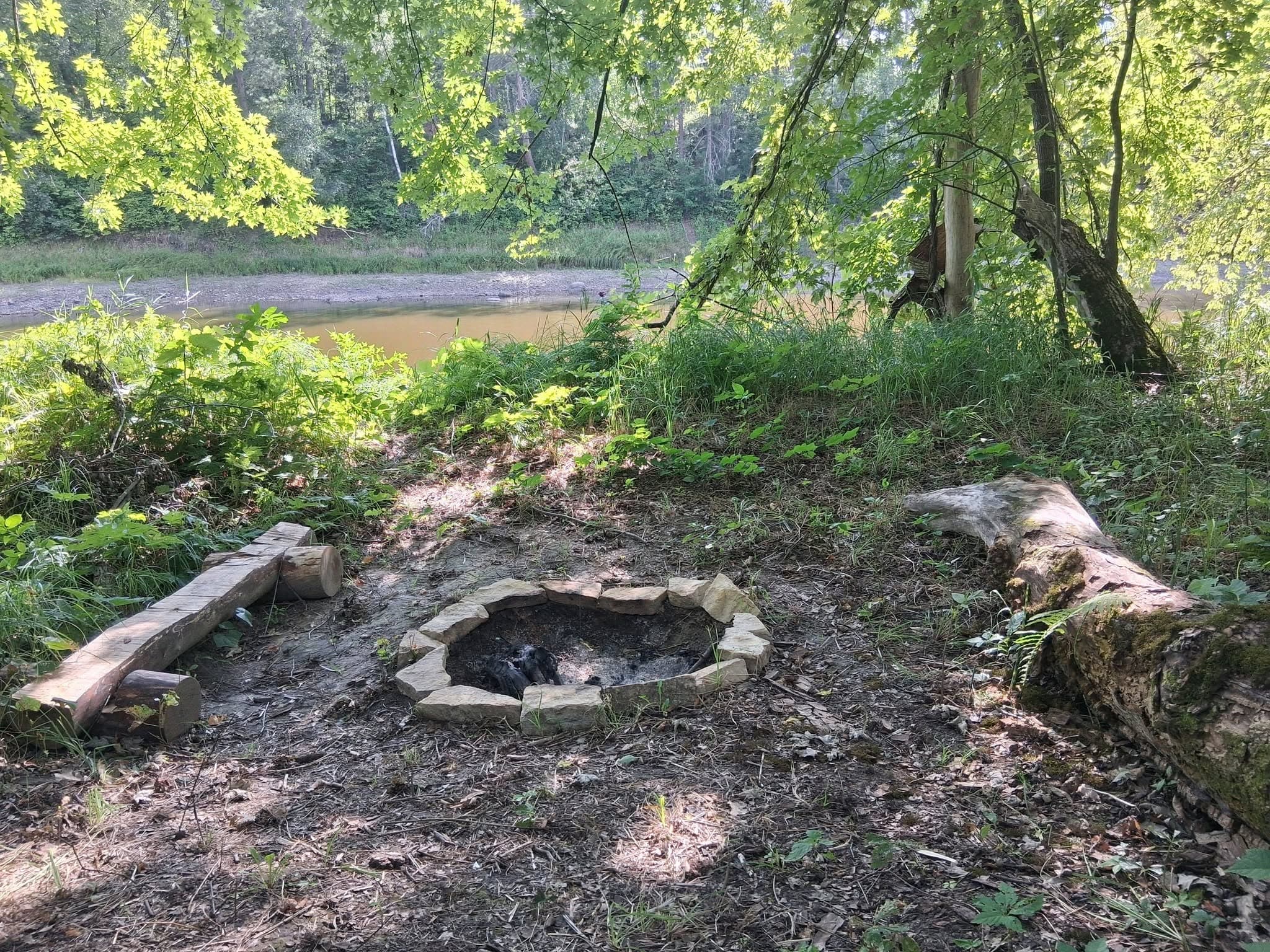 Stone campfire ring by the riverside with forested banks