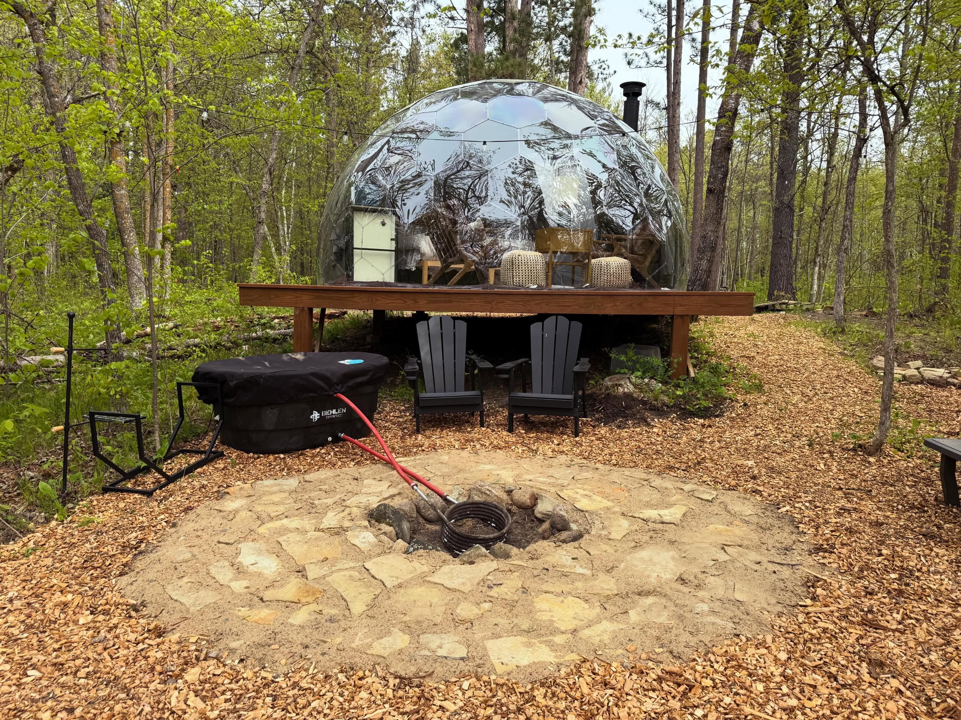 Geodesic dome on a wooden platform with fire pit and Adirondack chairs